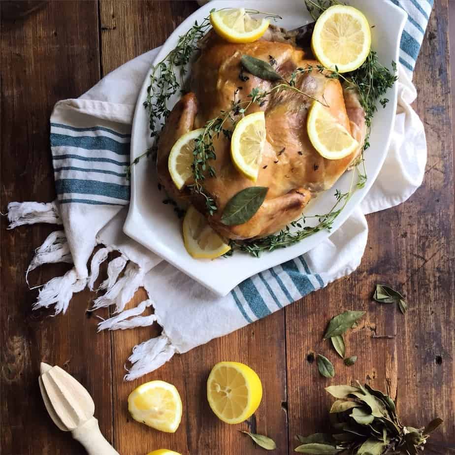 Ready Slow Cooker Lemon Thyme Whole Chicken on a wooden table, decorated with a white towel underneath the plate
