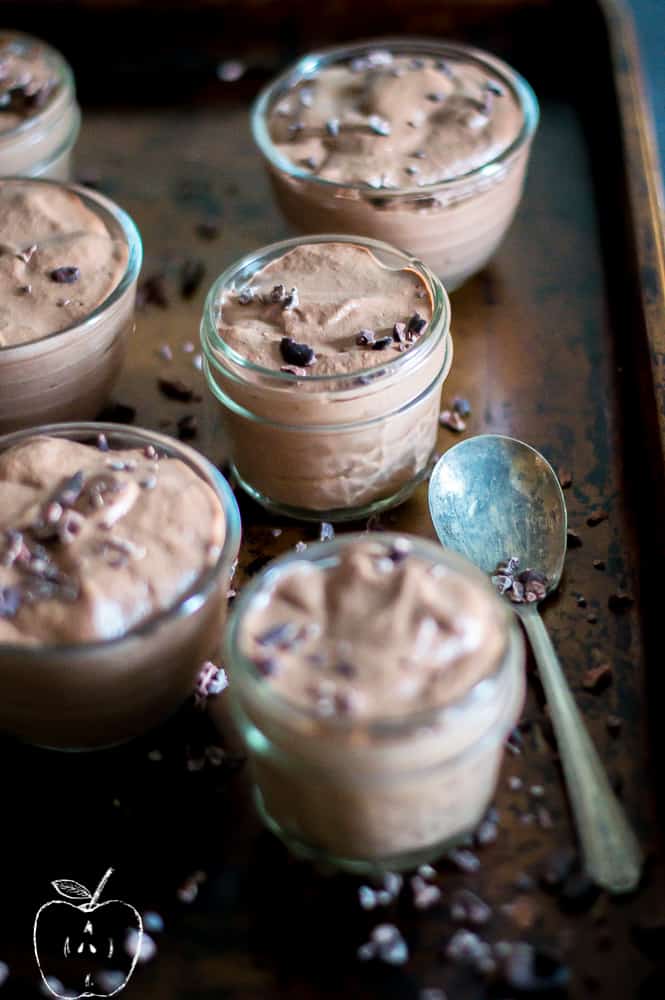 Closeup of the delicious chocolate chia pudding served in a jar with plenty of other jars blurred around it and a metal spoon inside a brownish metal tray