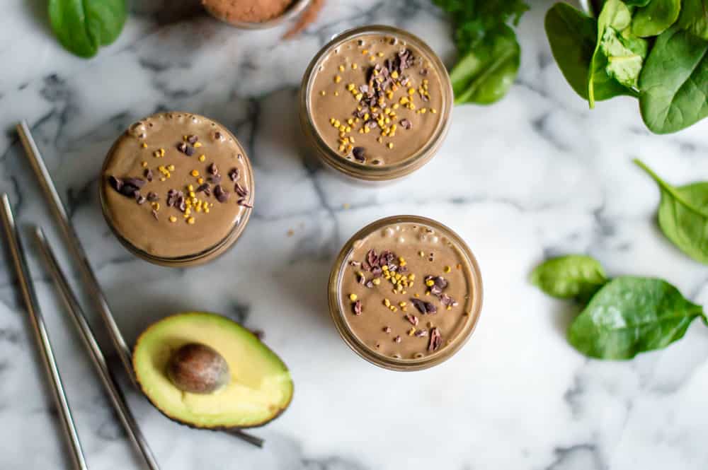 Overhead on the Healthy Peanut Butter Chocolate Smoothie served in three jars with a fresh avocado next to the jars