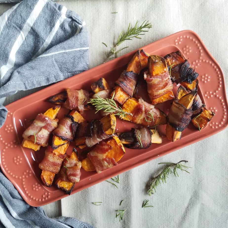 A big beautiful tray full of the delicious bacon wrapped sweet potatoes decorated with a sprig of rosemary