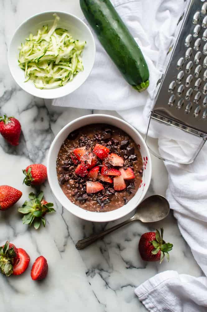 Zucchini chocolate oatmeal served for breakfast with lots of fresh produce around the bowl.