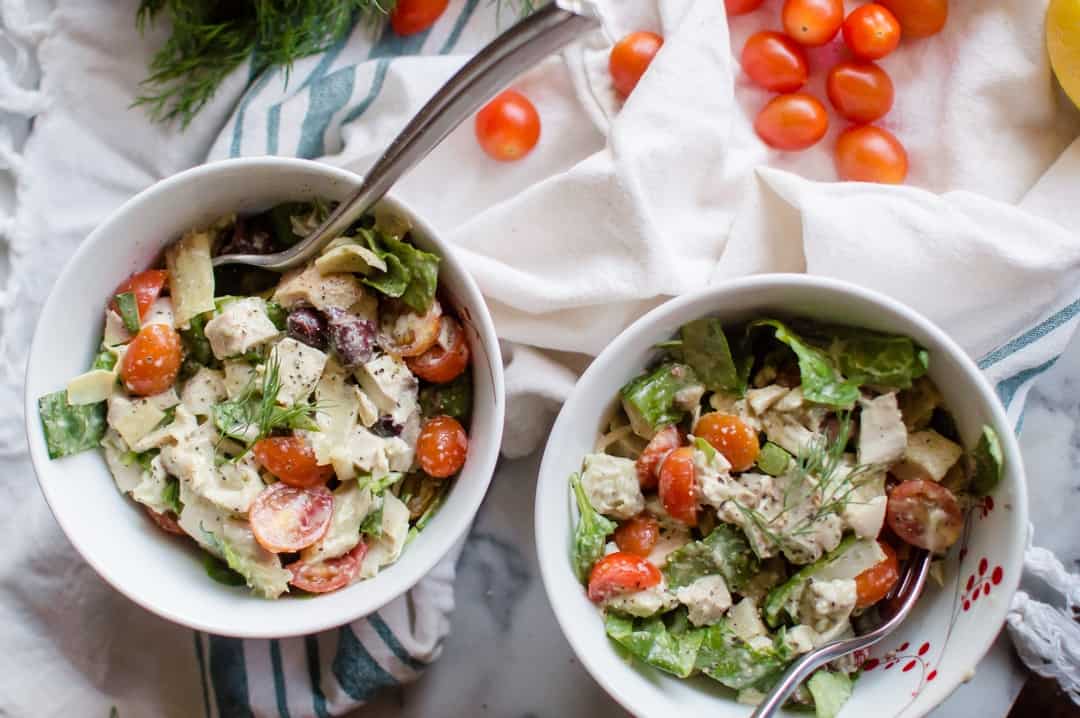 Two bowls of Whole30 Greek Chicken Salad on a big white towel on a marble surface