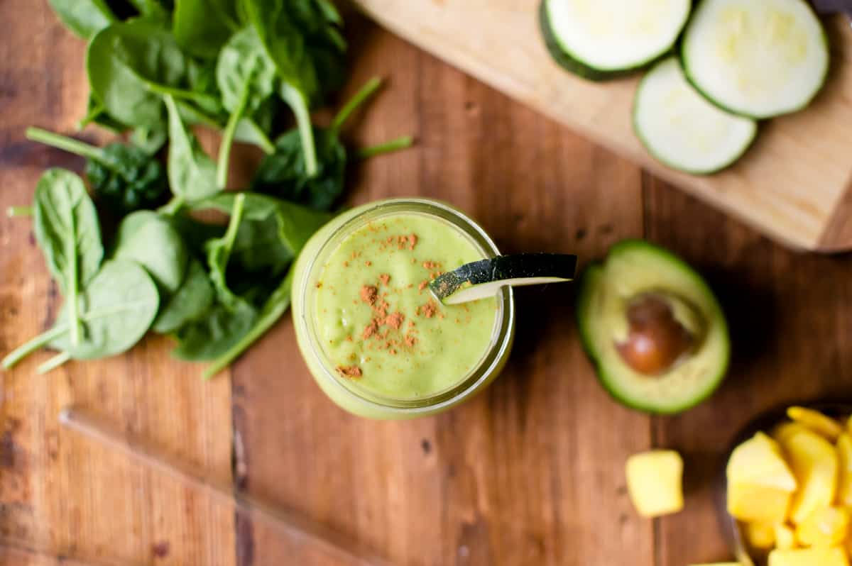 An overhead shot of zucchini avocado smoothie on a table with the ingredients surrounding it.