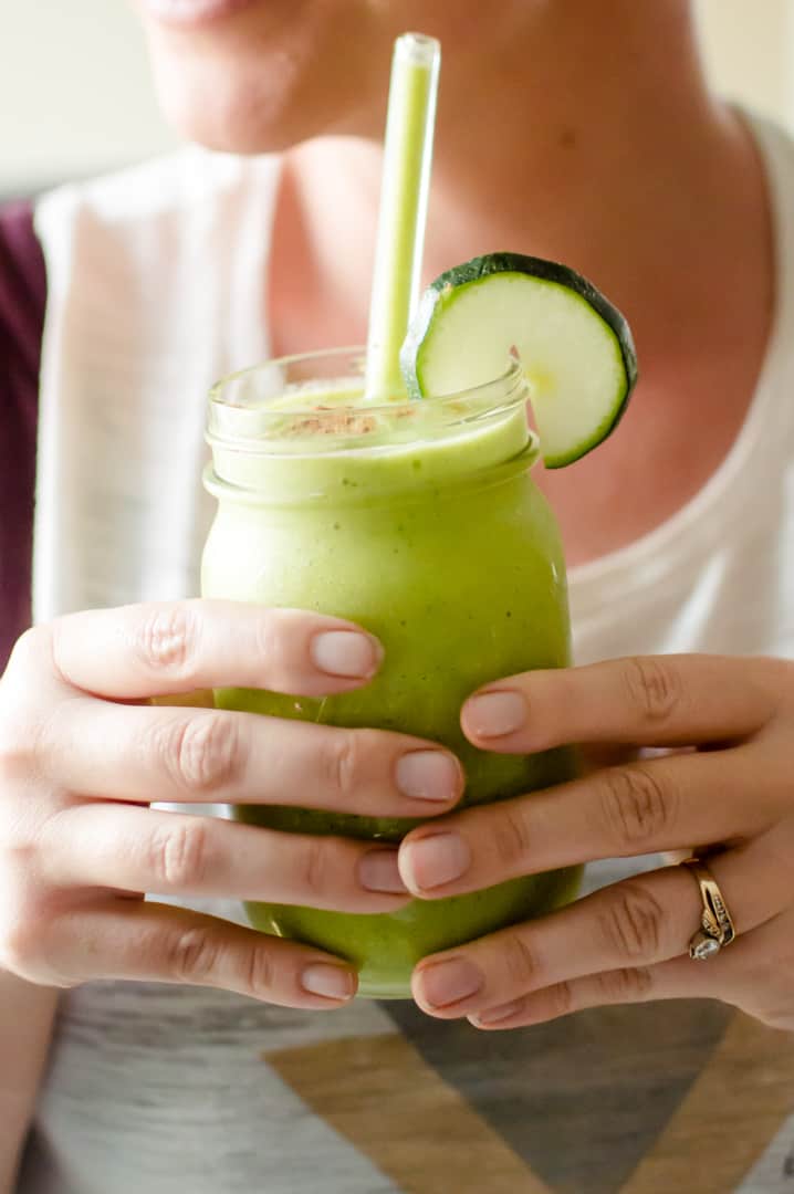 Two hands holding a glass of zucchini avocado smoothie.