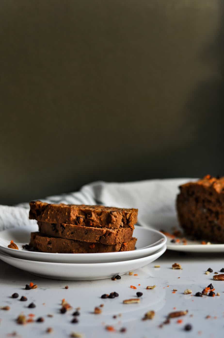 Side view of the chocolate chip carrot bread tower in two white plates with more bread blurred in the background.