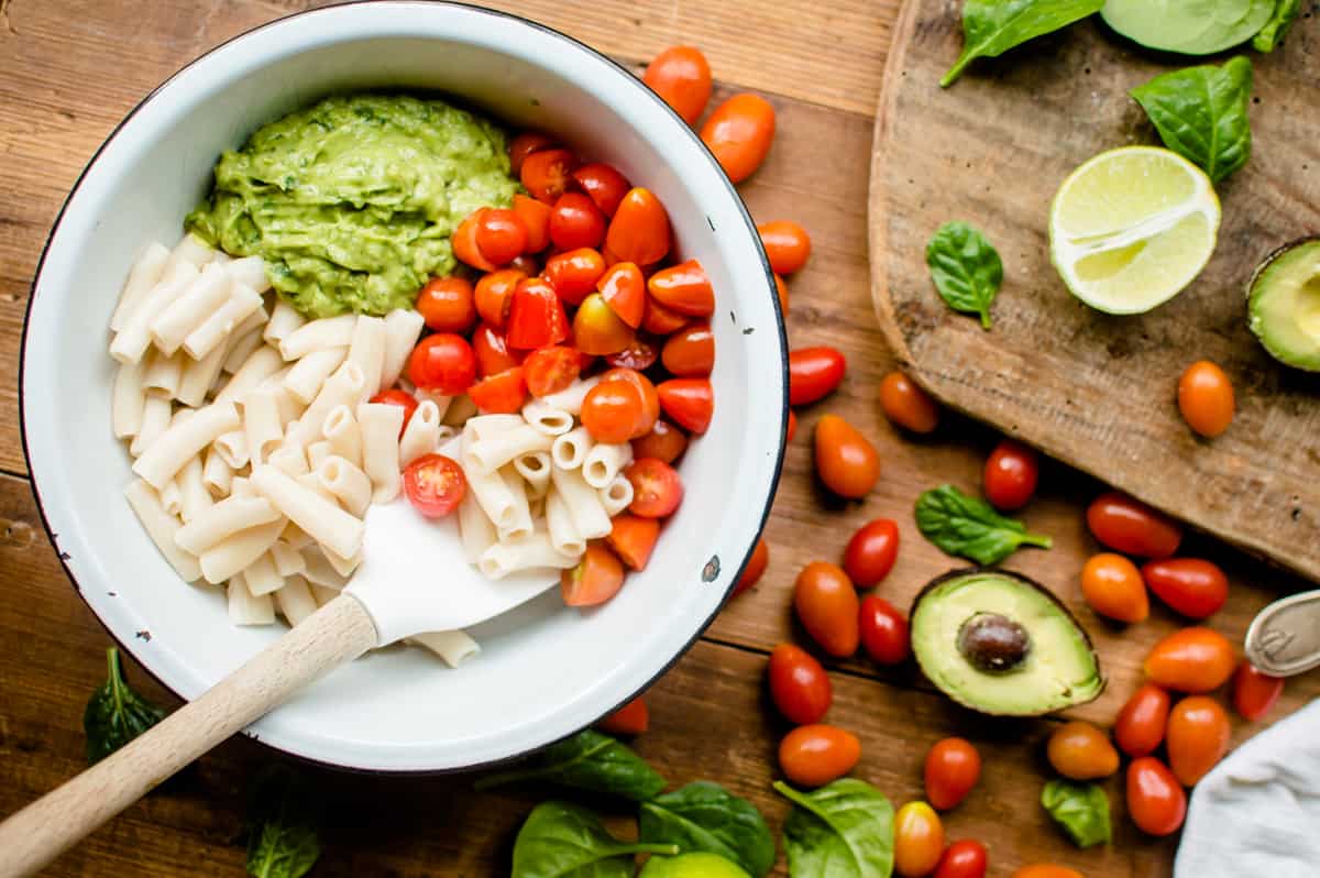 Overhead on the ingredients inside a big white bowl with plenty of tomatoes and avocados right next to it on the table