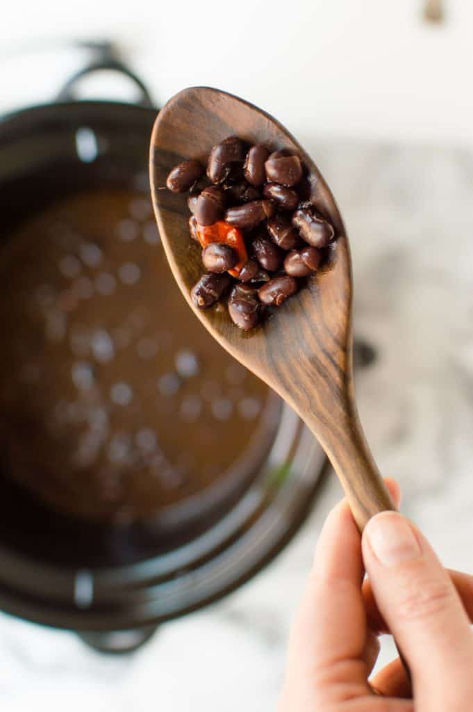 Slow cooker black beans after they have been cooked. Image is a close up of a wooden spoon containing a scoop of cooked beans. 