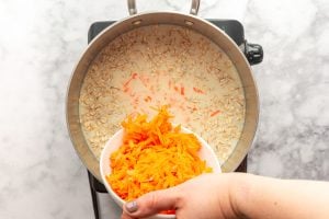 Grated carrots being poured into a pot with milk and rolled oats.