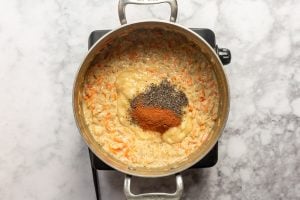 Carrot oatmeal in a pot with mashed banan, chia seeds, and cinnamon sitting on top before being stirred in.