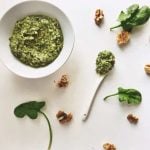 Overhead on the healthy and yummy Creamy Spinach Walnut Pesto in a white bowl and a spoon with plenty of walnuts around