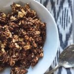 Closeup of the delicious Chocolate Coconut Granola served in a big white bowl with a spoon on the side