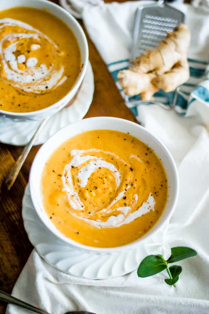 Two bowls full of the healthy and delicious Carrot Ginger Soup with raw ginger on the side on top of a white towel