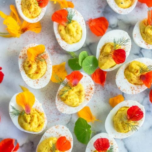 Overhead on plenty of delicious turmeric deviled eggs decorated with beautiful petals and looking extra bright and yummy