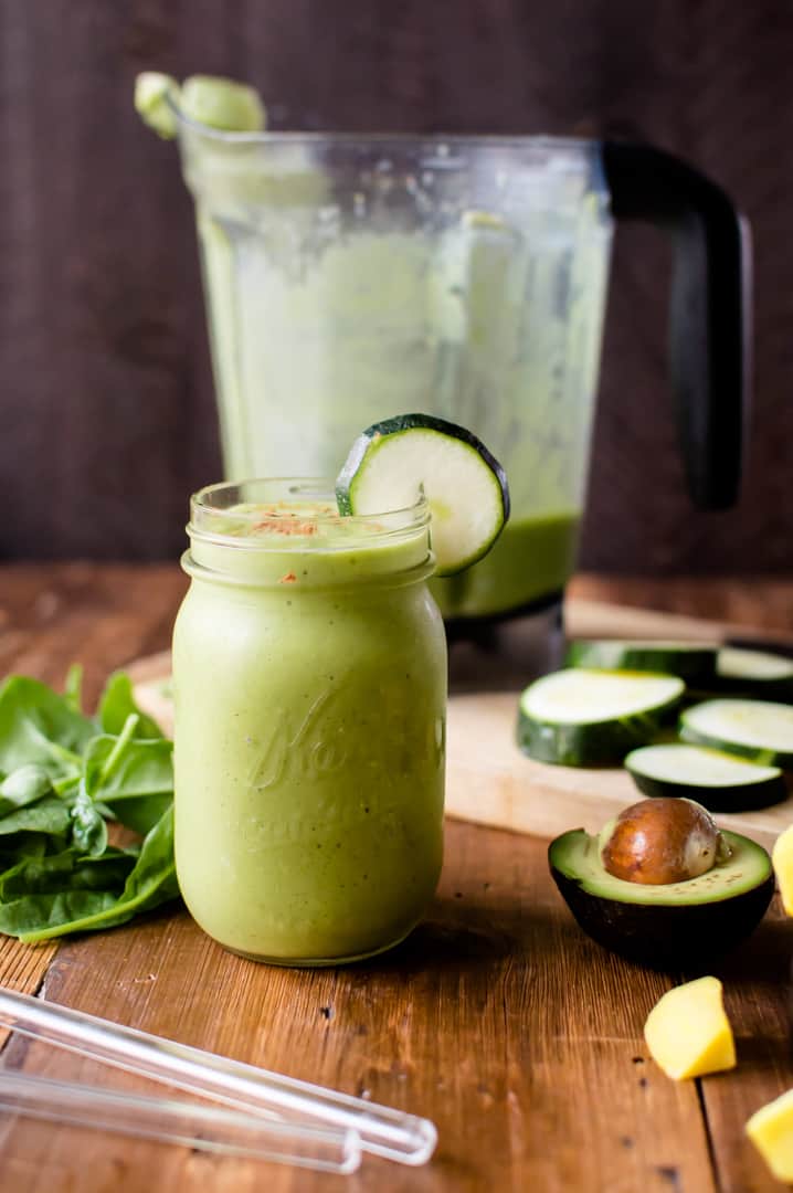 A glass of zucchini avocado smoothie on a table with the blender blurred in the background. 