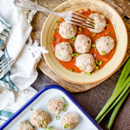 Delicious Chicken Cauliflower Meatballs served in a big cute bowl with a forn on top and a white tray with more meatballs on a wooden board