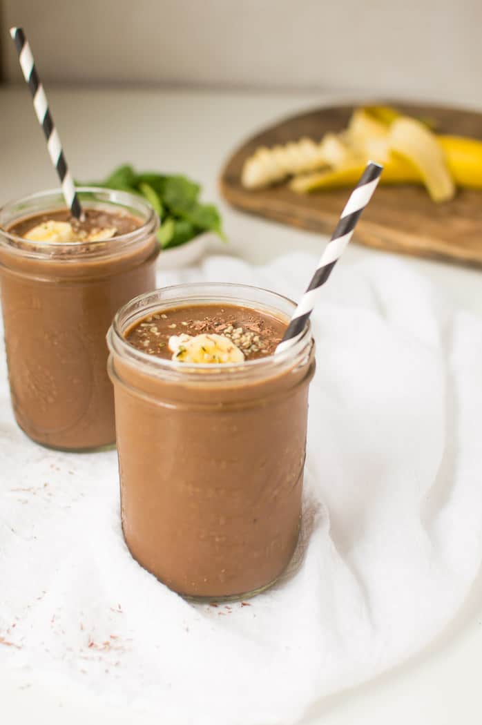 Incredibly inviting chocolate banana smoothie jars with two striped straws as well as banana skins blurred in the background