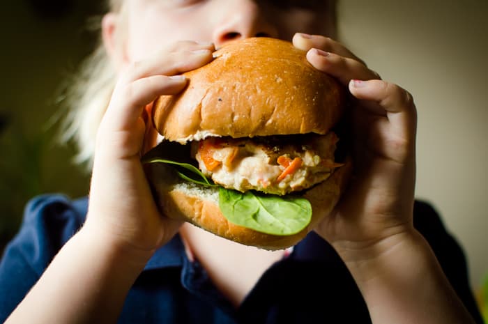 A child holding a healthy turkey burger in a bun in front of her face.