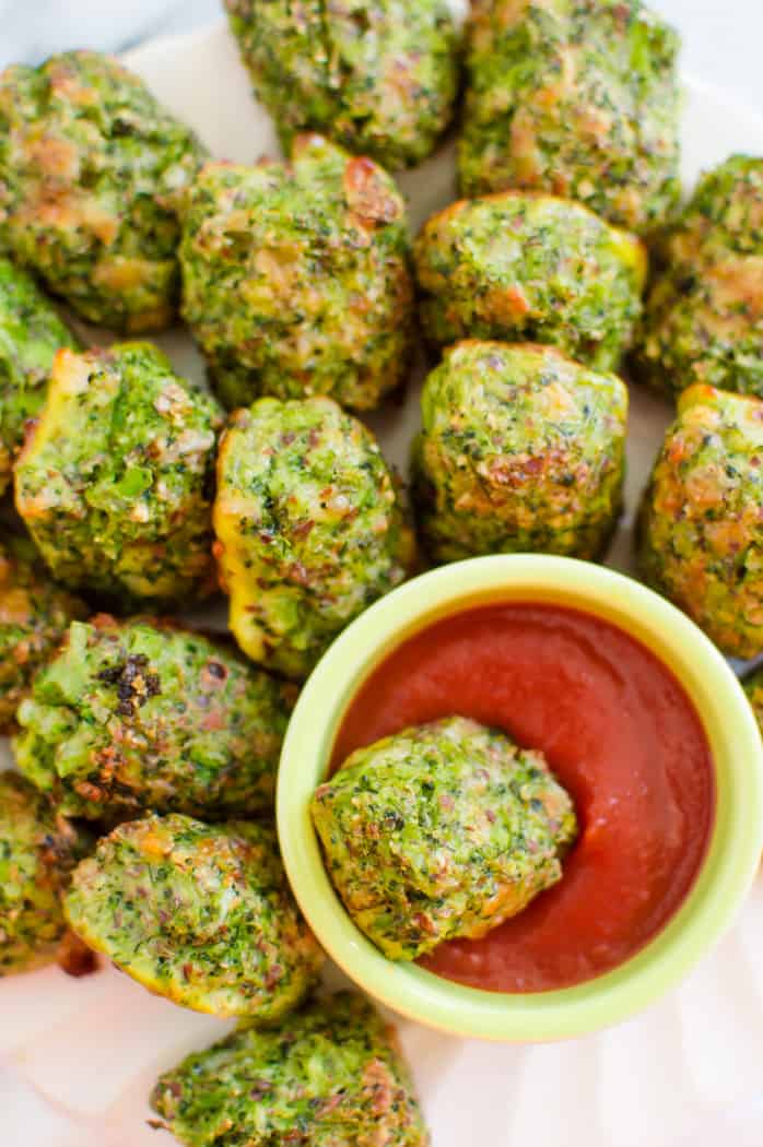 Broccoli tots on a plate with a bowl of ketchup. One tot is in the bowl with the ketchup. 