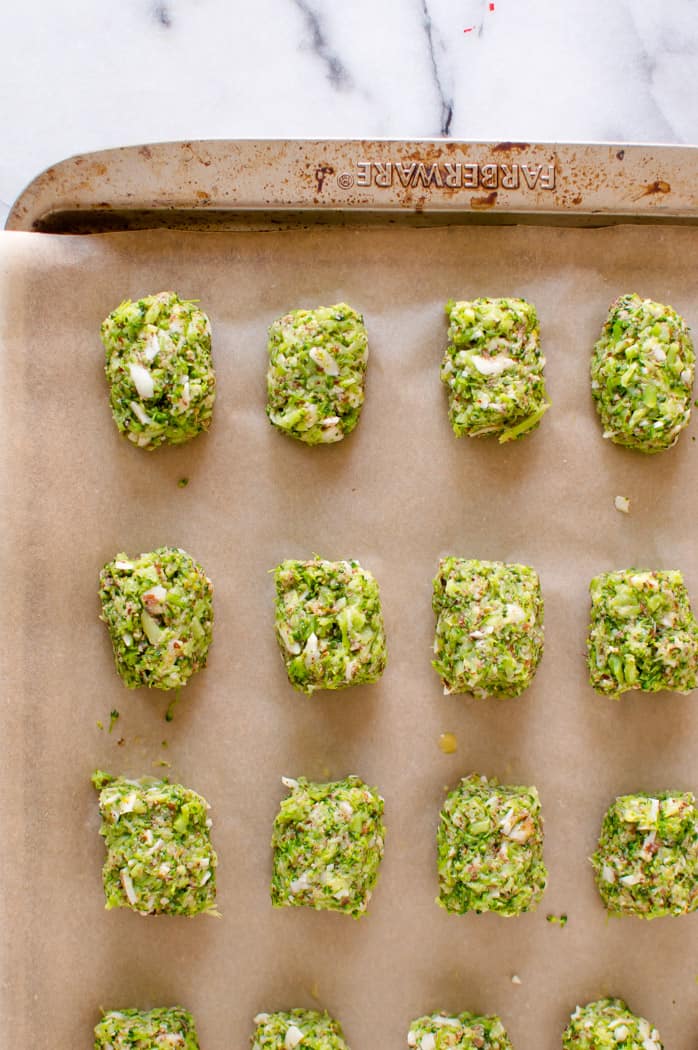 Formed, uncooked broccoli tots on a lined baking sheet before baking