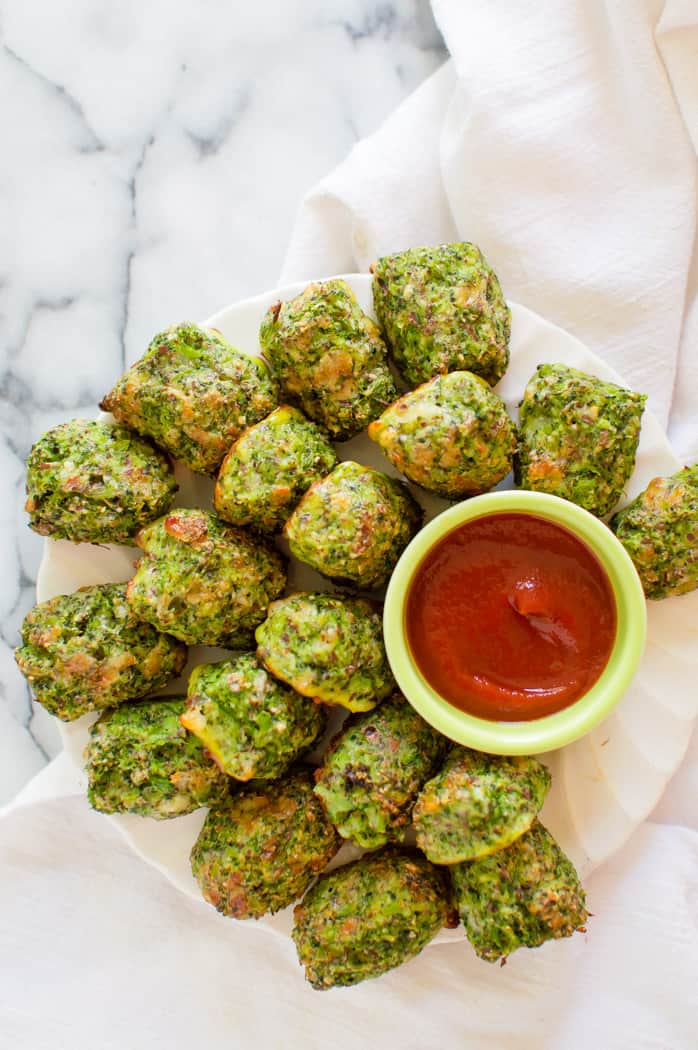 Cooked broccoli tots on a plate with a bowl of ketchup.