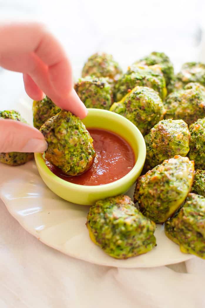 A hand dipping a broccoli tot into a bowl of ketcup.