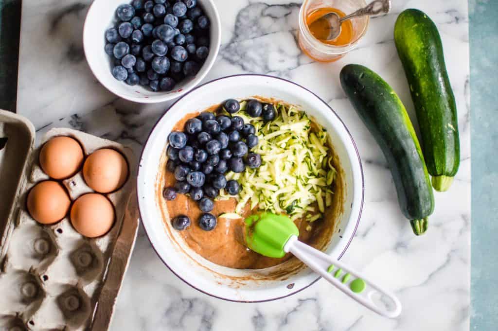 Combining all recipe ingredients in a big bowl: eggs, blueberries, zucchini and honey; mixing them well and getting ready for baking.