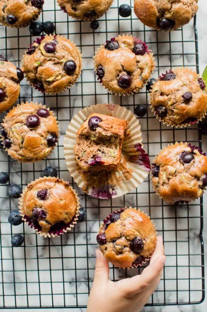 A kid's right hand holding a blueberry zucchini muffin - one of the 15 healthy muffin recipes for kids
