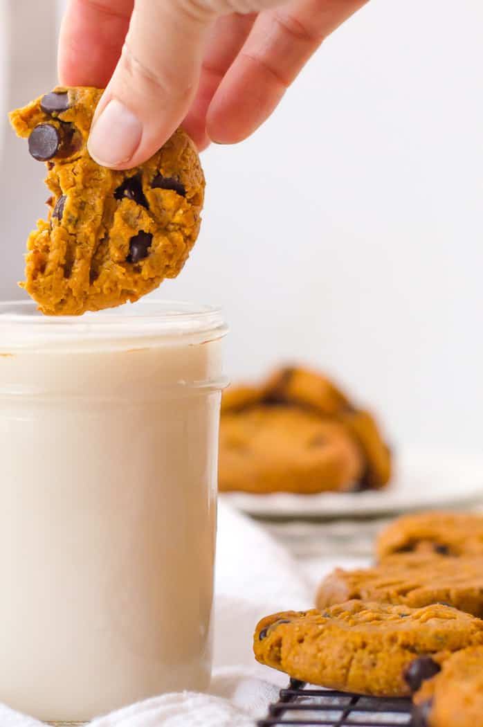 Dipping one of the Vegan Peanut Butter cookies into a big glass of milk with one bite already missing.