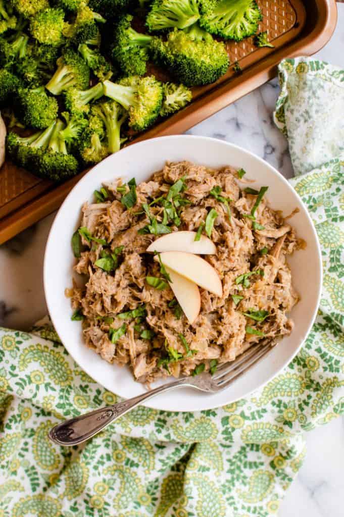 A bowl of pulled pork next to a try of roasted broccoli