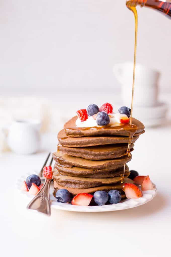 A stack of veggie-loaded chocolate pancakes with syrup being poured over it