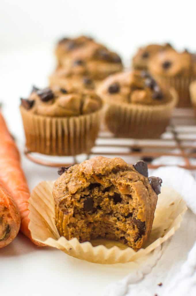 A vegan carrot muffin with a bite taken out of it, with the other muffins cooling in the background
