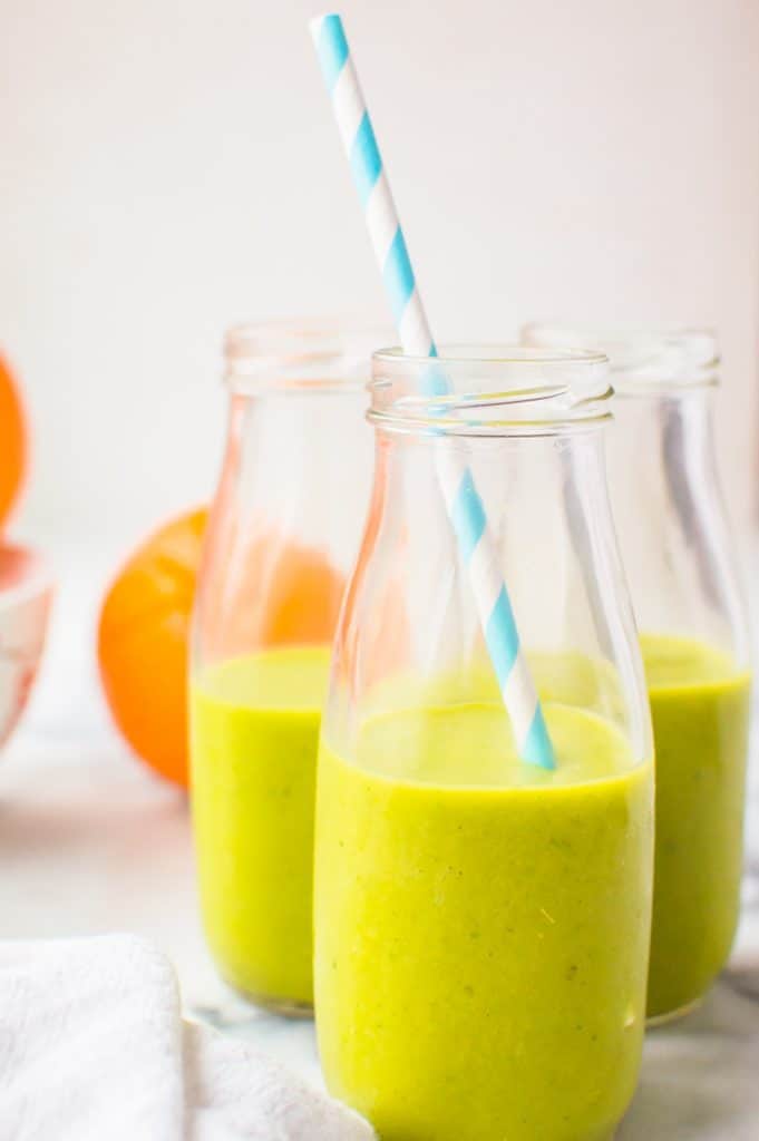 A simple green smoothie for kids in a glass with a straw with glasses of smoothie in the background