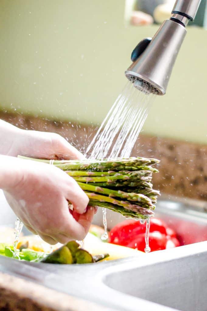Hands rinsing asparagus after is has soaked in homemade fruit and veggie wash.