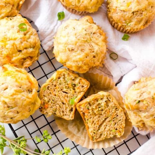 Savory Vegetable Muffins on a cooling rack with a white tea cloth, with one muffin is cut open to show the texture of a cooked muffin