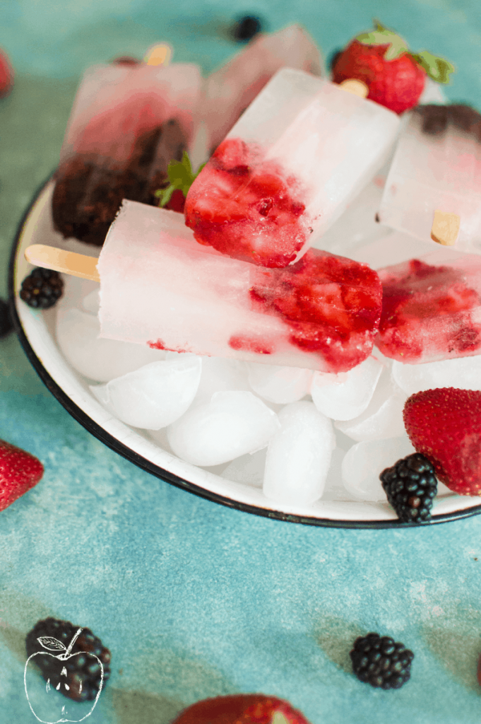 Berry hydrating popsicles in a bowl of ice with berries scattered around. 