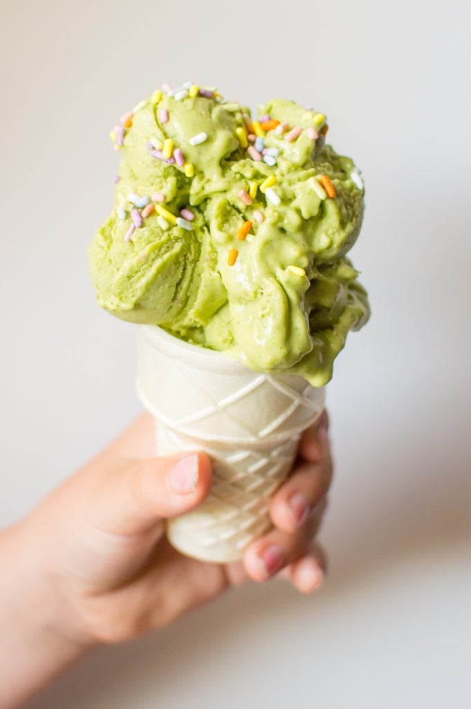 Green smoothie nice cream in a cone with a child's hand holding it. 