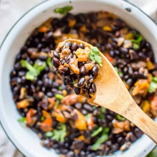 A spoonful of the delicious and healthy Instant Pot Black Beans with a big white bowl blurred in the background