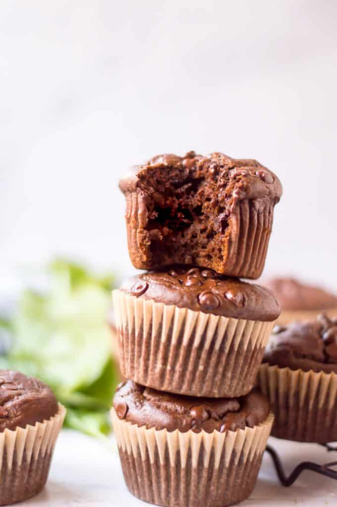Three veggie-loaded healthy chocolate muffins stacked on top of one another. The top muffin has a bite out of it. 