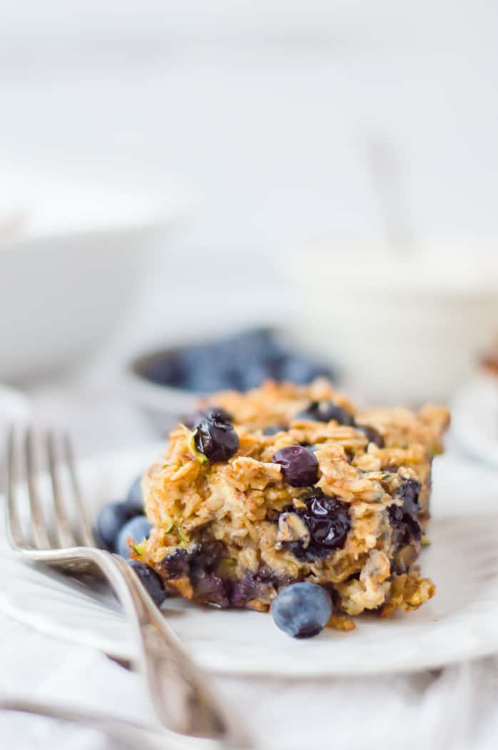 A piece of blueberry zucchini oatmeal on a plate with fresh berries and a fork. 