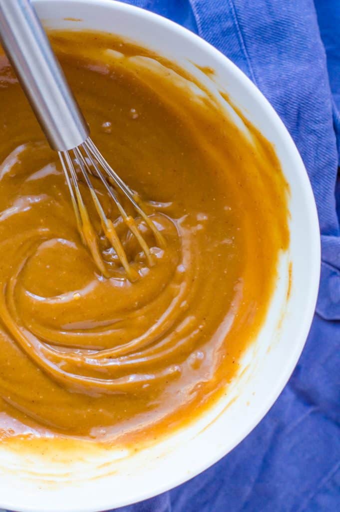 easy peanut sauce in a bowl with a whisk, mixed up. There is a blue napkin under the bowl. 