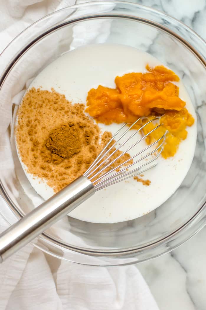 Milk, maple syrup, pumpkin pie spice and pumpkin puree in a bowl with a whisk before mixing.  