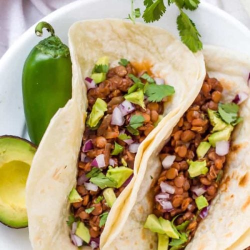 Vegan Slow Cooker Lentil Tacos served with peppers and avocado on the side of the plate.