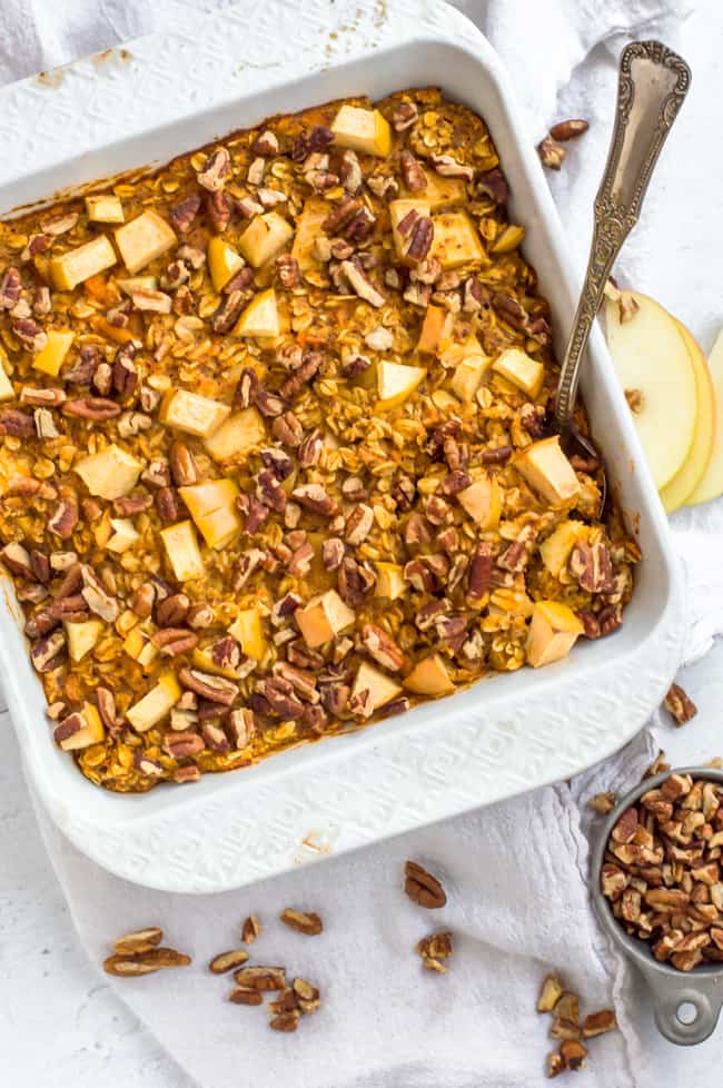 Apple sweet potato baked oatmeal in a baking dish with a spoon. A bowl of nuts are next to it. 