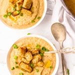 Overhead on two bowls with cauliflower vegetarian potato soup served with croutons and two metal spoons