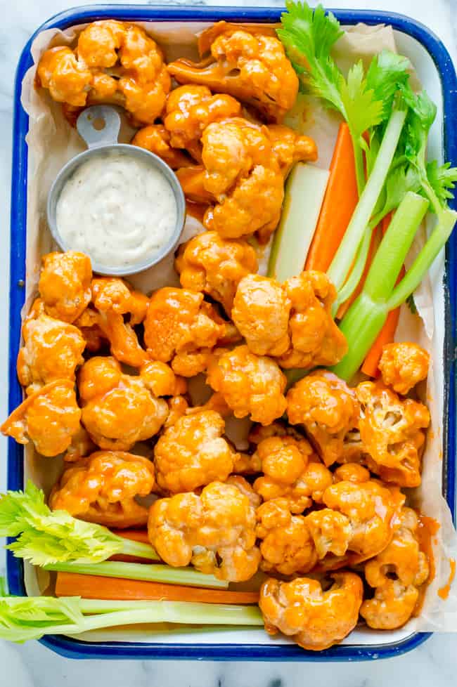 A tray of buffalo cauliflower wings with carrots and celery sticks and a bowl of ranch.