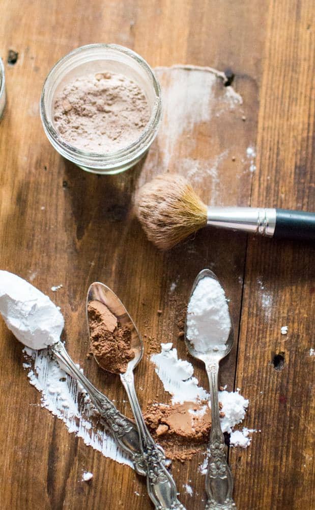 The ingredients for DIY dry shampoo in spoons and then mixed together in a jat with a brush next to it.