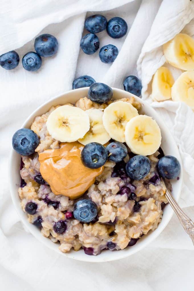 A bowl of blueberry cauliflower oatmeal topped with fresh blueberries, bananas and some peanut butter