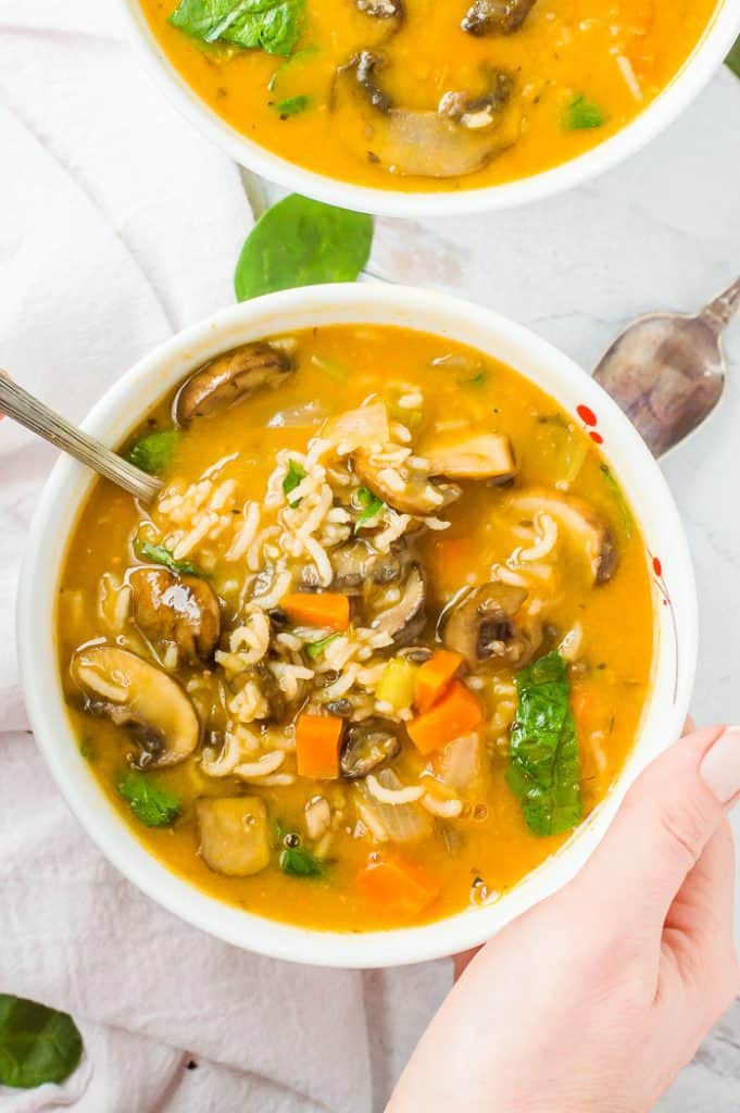 Mushroom vegetable soup in a bowl. And hand is on the side of the bowl 