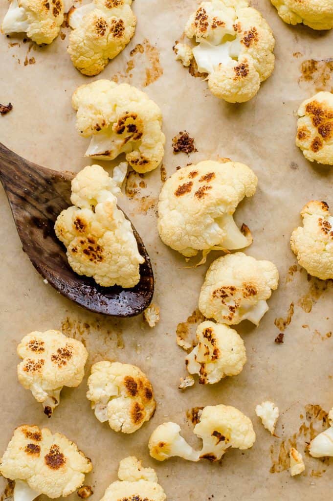 Roasted cauliflower florets on a baking sheet with a spoon.