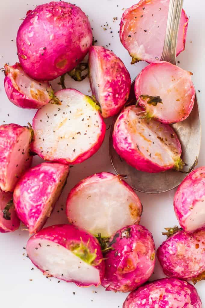 Roasted radishes in a bowl with a spoon. They are sprinkled with pepper.